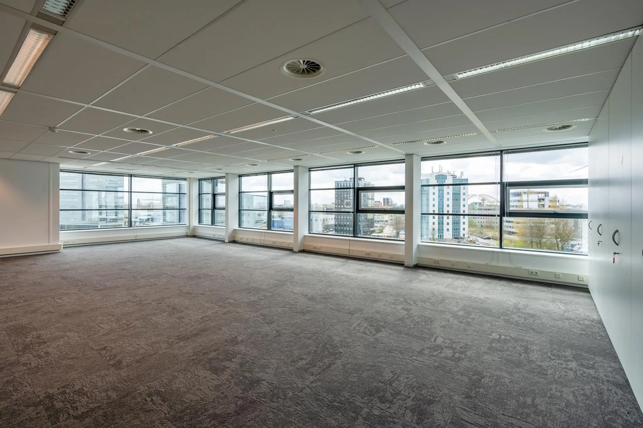 Lichte, lege kantoorruimte met grote ramen en uitzicht op de gebouwen aan de Fascinatio Boulevard.